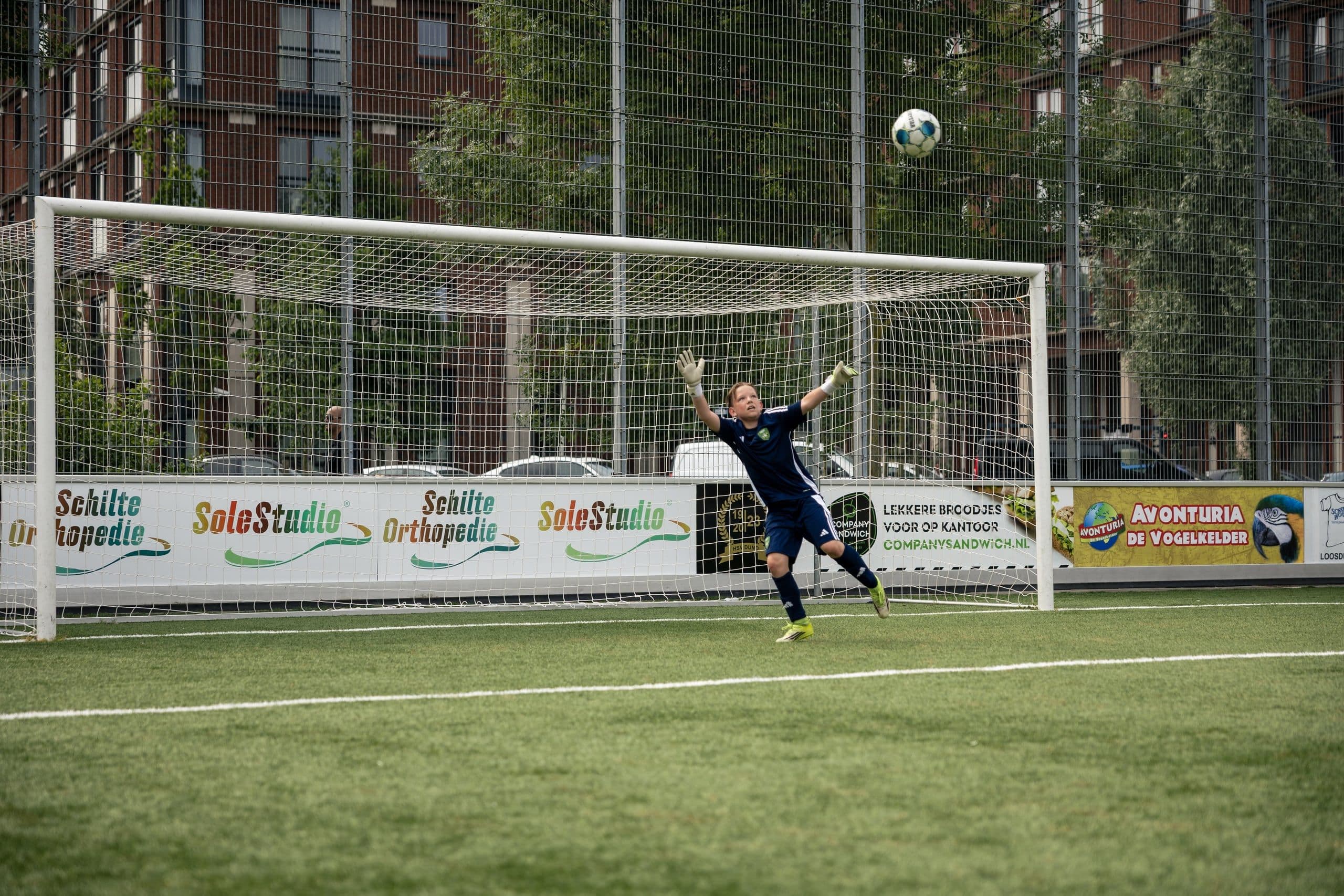 Jeugdkeeper springt naar de bal tijdens een keeperstraining.